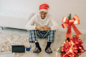 Wall Mural - man with santa claus hat at home with mobile phone and computer
