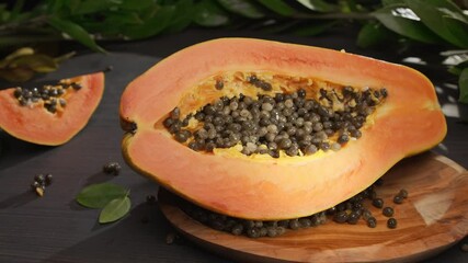 Wall Mural - Half papaya fruit with seeds on a vintage table with leaves of tropical plants. A hand puts a piece of papaya on a bowl of fruit. Horizontal slow movement of the camera from left to right. 