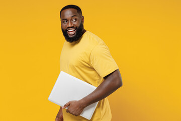 Wall Mural - Young smiling copywriter fun happy black man 20s wearing bright casual t-shirt hold use closed laptop pc computer isolated on plain yellow color background studio portrait. People lifestyle concept.