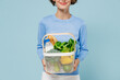 Cropped young cool woman 20s in casual sweater look camera hold white busket with begetables ingredients isolated on plain pastel light blue background studio portrait. People lifestyle food concept.