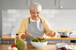 © Syda Productions - healthy eating, food cooking and culinary concept - happy smiling senior woman making vegetable salad on kitchen at home