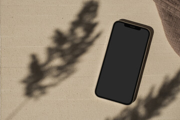 flatlay phone in flowers sunlight shadows on neutral beige background. aesthetic elegant blog, socia