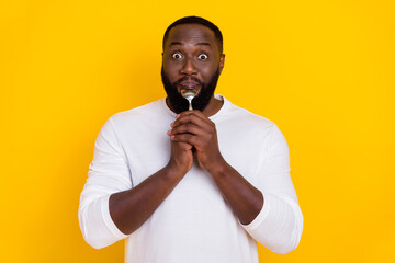 Wall Mural - Portrait of excited crazy guy hold lick spoon have good mood look camera isolated on yellow color background