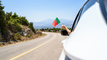 Wall Mural - Woman holding Portugal flag from the open car window driving along the serpentine road in the mountains. Concept