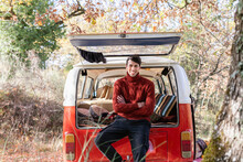 Smiling Young Man With Arms Crossed Sitting At Campervan