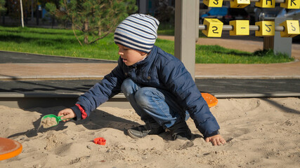 Wall Mural - Little boy playing in sandpit on palyground and building sand castle. Concept of child development, sports and education.