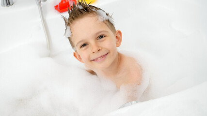 Wall Mural - Portrait of happy smiling boy washing in bath with soap suds and looking in camera. Concept of hygine, children development and fun at home