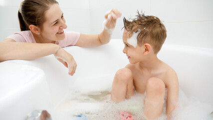 Wall Mural - Happy smiling mother playing with her son washing in bath with soap foam. Concept of family time, children development and fun at home