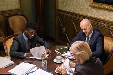 Sticker - Group of contemporary intercultural lawyers looking through papers while sitting by table in boardroom