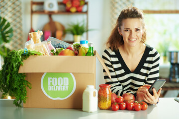 Wall Mural - smiling housewife using smartphone recipes app in kitchen