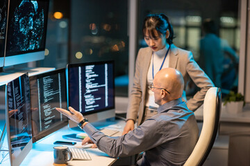 Sticker - Two intercultural colleagues interacting in front of computer monitors with coded data while one of them making presentation