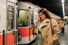 Smiling Woman In Overcoat Using Mobile Phone At Railroad Station