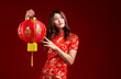 Beautiful young Asian woman in chinese traditional cheongsam qipao dress holding a Chinese lantern isolated on red background. Chinese new year concept