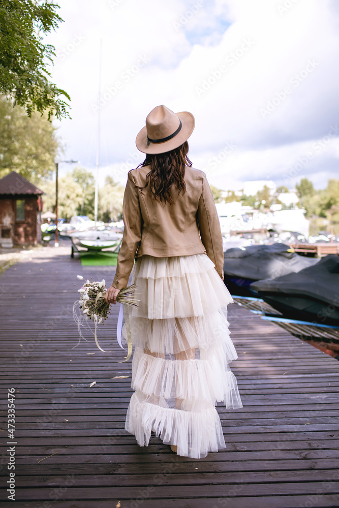 Stylish bride with a wedding bouquet is walking along the wooden bridge. A  young bride is