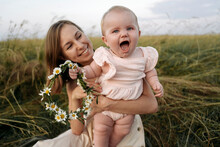 Smiling Mother Holding Cheerful Baby Girl With Flower Tiara In Field