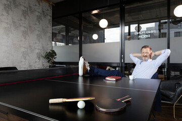 Businessman with hands behind head sitting at table tennis table in office