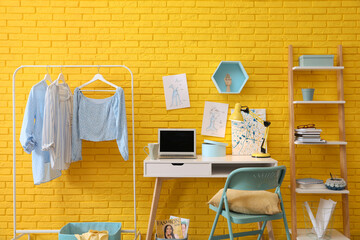 Poster - Fashion designer's workplace with wooden furniture and laptop near yellow brick wall. Stylish interior