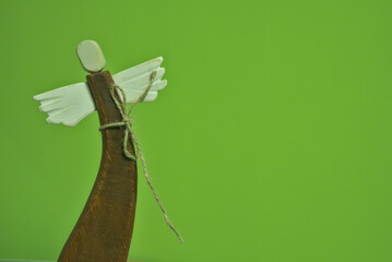 wooden angel with white wings. old angel figurine in a curved pose on a green background. isolated from background. a minimalistic Christmas decoration with a solid background, with space for text