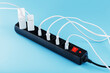 Black surge protector with a red button and connected white wires of electrical appliances on a blue background.