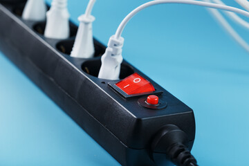 Black surge protector with a red button and connected white wires of electrical appliances on a blue background.