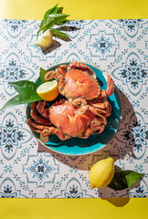 Wall Mural - Cooked crab on blue plate, lemons, rose wine on table, sunlight immitation