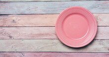 Empty pink plate on pastel wooden background for Easter. Food background for menu, recipe book. Table setting. Flat lay, top view, mock up