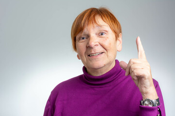 Wall Mural - Cheerful senior woman pointing finger up.