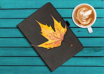 Poster - a cup of tea and a book on a wooden surface against the background of fallen leaves, autumn season