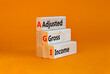 AGI adjusted gross income symbol. Concept words AGI adjusted gross income on wooden blocks. Beautiful orange table, orange background, copy space. Business and AGI adjusted gross income concept.