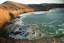 Waves Flowing Between Rocks Against Ocean Cliffs In Bay At Sunset