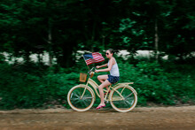 Girl Riding Her Bike With An American Flag On A Rural Dirt Road