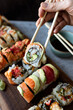 © Cavan Images - Close up of hand holding sushi roll using chopsticks above a platter.
