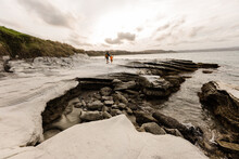 Father And Child Walking On Rocky Shore Near Ocean In New Zealand