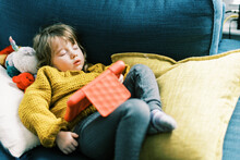 Little Toddler Girl In Primary Colors Sleeping On Sofa With Tablet