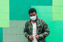 Afro American Black Boy On Green Wall Background. Dressed In Military Jacket And Face Mask.
