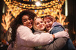 © Cavan Images - Happy female friends embracing standing by Christmas lights in city