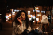 © Cavan Images - Young women eating street food standing by table in city at night
