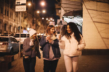 Happy Female Friends Having Hot Drinks Walking On Street In City
