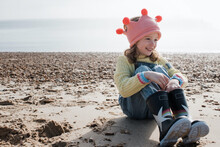 Girl Sat Smiling On The Beach Wearing A Crown On A Sunny Day In The UK