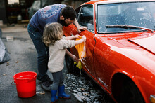 Little Girl Cleaning A Red Classic Car With Her Father Together