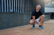 © Kostiantyn - Middle aged sportsman looking away while tying shoelaces on his blue running sneakers, getting ready for workout outdoors