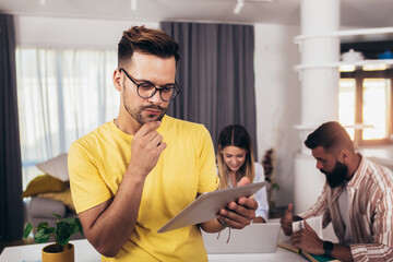 Portrait smart confident smiling man standing at home using digital tablet with friends in background