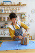 © DimaBerlin - Happy female artist packing gift with handmade pottery after master class in ceramic studio. Young woman entrepreneur packaging for delivery handicraft tableware. Small business and art shop ownership