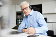 © Westend61 - Male professional with wireless headset writing in book at office