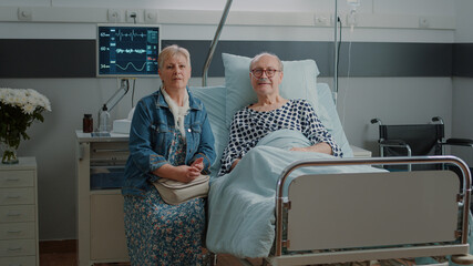 portrait of senior man in hospital ward bed receiving assistance from wife, waiting on medical advic
