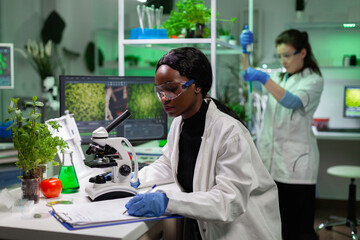 Wall Mural - african american chemist woman writing medicine experiment results on clipboard after analyzing gene