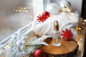 Cosmetic oil bottle on christmas window background. Beauty flat lay with christmas decorations