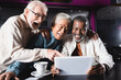 © LIGHTFIELD STUDIOS - amazed senior man pointing at digital tablet near cheerful multiethnic friends in cafe