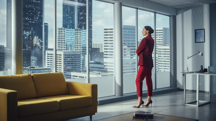 Wall Mural - Successful Thoughtful Businesswoman Wearing Perfect Red Suit Standing in Office Looking out of Window on Big City. Confident Female Corporate Top Manager of IT Company Plans Investment Strategy