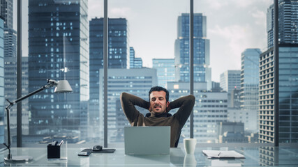 Poster - Portrait of Relaxed Brilliant Businessman Working on Laptop Computer in His Big City Office. Charismatic Laid-back Entrepreneur Leaned Against the Back of the Chair and Chill.
